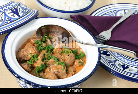 Un bol de service de bœuf stroganoff avec du riz blanc et une cuillère sur une table et assiettes et fourchettes Banque D'Images