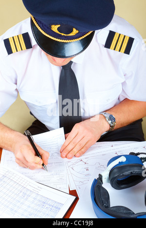 Pilote de ligne souriant wearing hat, chemise avec épaulettes et cravate avec stylo à la main prêt à remplir des papiers et de contrôle p vol Banque D'Images