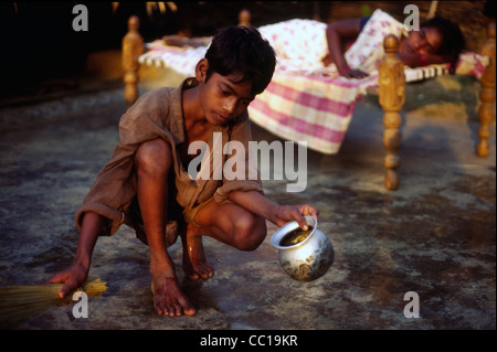 Un garçon se lave et balaie le plancher tandis que sa mère se trouve sur un charpoy, Andhra Pradesh, Inde Banque D'Images