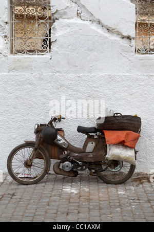 Et plutôt ancienne mono-cylindre rouillé moto ou cyclomoteur appuyé contre un mur blanc à El Jadida, Maroc Banque D'Images
