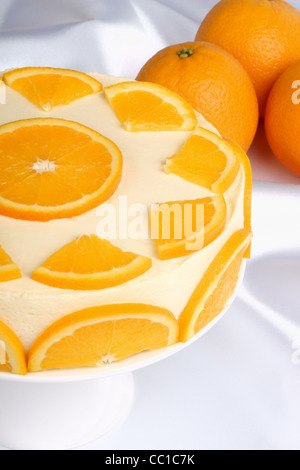 Crème bavaroise (bavarese orange) sur un stand de gâteau en porcelaine blanche et quelques oranges dans l'arrière-plan. Focus sélectif. Banque D'Images