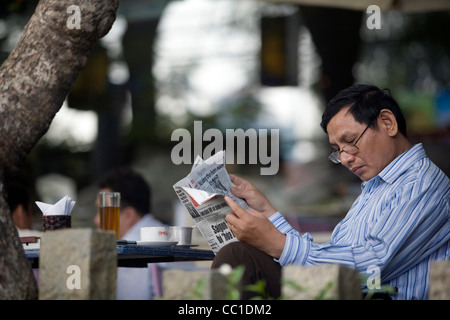 Un homme lit un journal dans un café haut de gamme à Ho Chi Minh Ville (anciennement Saigon) Vietnam Banque D'Images