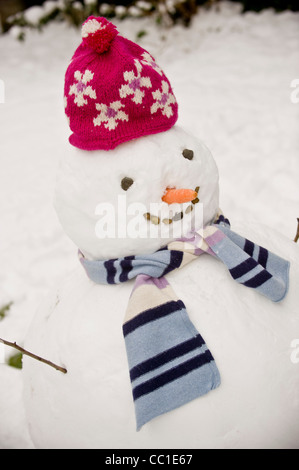 Bonhomme de neige portant un chapeau en laine rose et une écharpe strippy dans un jardin britannique. Banque D'Images