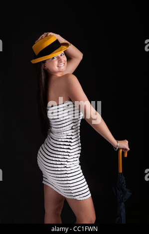 Belle jeune femme en mini jupe avec chapeau jaune sur fond sombre Banque D'Images