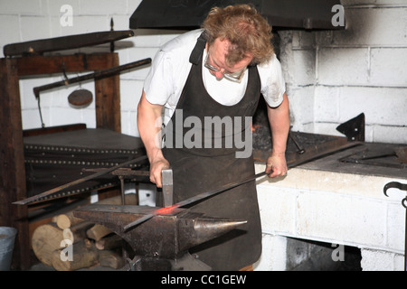 Le travail des métaux de forgeron sur l'enclume dans sa forge. L'Irlande Banque D'Images