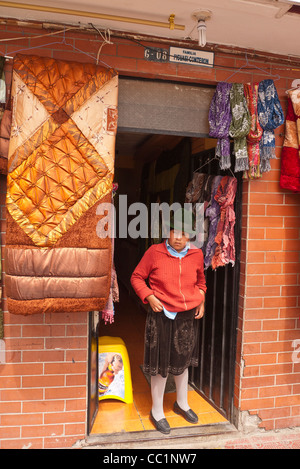 Une femme indienne andine dans la vingtaine se tient à la porte de son magasin à Otavalo, Equateur. Banque D'Images