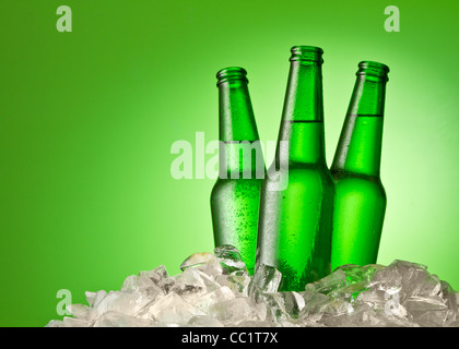 Trois bouteilles de bière se refroidir dans la glace. Isolé sur un vert. Banque D'Images