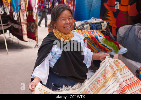 Une femme indienne sourit tout en montrant un tapis tissé à la vente sur le marché intérieur de l'Otavalo, Équateur. Banque D'Images