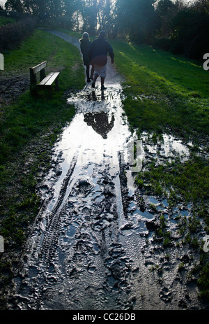 Couple en train de marcher avec précaution sur le chemin boueux, reflété dans une flaque d'eau, contre la lumière Banque D'Images