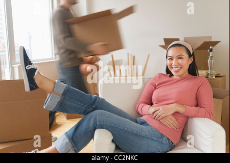 USA, New Jersey, Jersey City, Man carrying boxes, woman resting in chair at new home Banque D'Images
