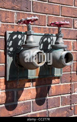 Vieille fontaine en cuivre avec deux soupape avec le vert-rouille et contre un mur de briques Banque D'Images