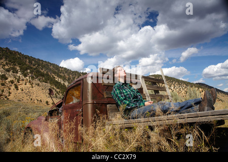 USA, Colorado, femme reposant sur lit de camion abandonné dans le désert Banque D'Images