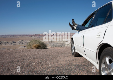 USA, Arizona, Winslow, Senior pieds hors de la fenêtre de voiture garée dans desert Banque D'Images