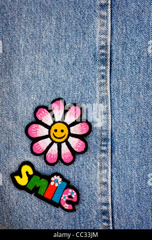 Fer à repasser la broderie sur les correctifs de sourire multicolore mot avec un smiley fleur sur un fond jean denim Banque D'Images