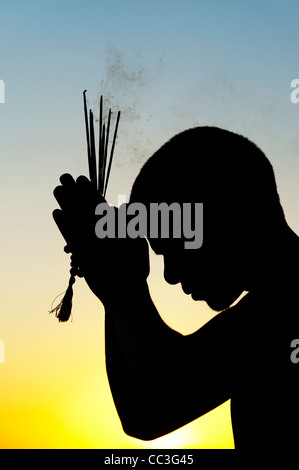 Priant avec encens indien au coucher du soleil. Silhouette. L'Inde Banque D'Images