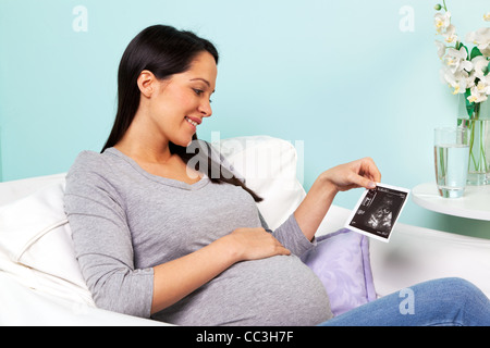 Photo d'une femme enceinte à la maison assis dans un fauteuil en regardant son bébé échographie imprimer. Banque D'Images
