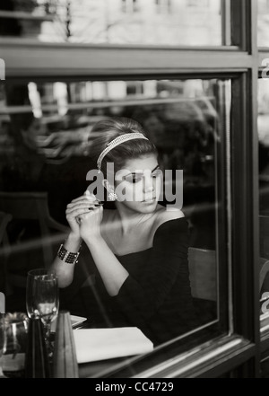 Une femme attend patiemment dans un restaurant alors qu'elle regarde par la fenêtre, en noir et blanc. Banque D'Images