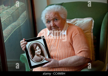 98 ans vieille dame tenant un ordinateur tablette iPad, affichant un portrait sépia d'elle-même pris il y a 80 ans à l'âge de 18 ans Banque D'Images