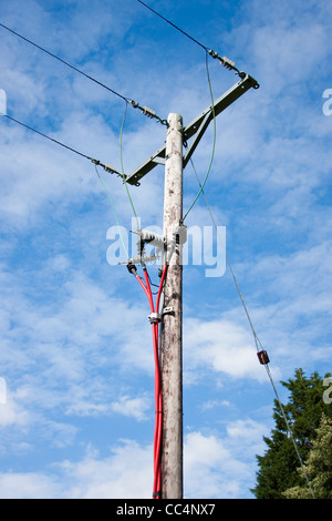 Pôle de l'électricité avec un rouge vif et des câbles aériens contre le ciel bleu Banque D'Images