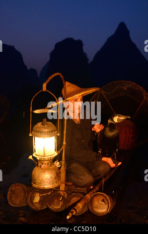 Cormoran pêcheur chinois tenant un oiseau sur un radeau en bambou avec lanterne à l'aube sur la rivière li avec des sommets de montagnes karstiques yangshuo chine Banque D'Images