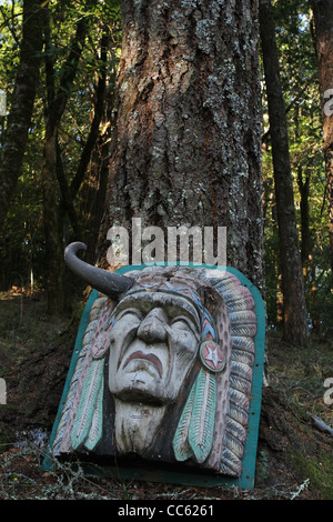 Une tête d'Indien en bois sculpté, appuyé contre un arbre dans une forêt. Banque D'Images