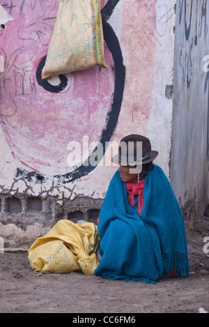 Une très vieille femme indienne andine est assis sur le sol près d'un mur de graffiti marqué Saquisili, Equateur, Amérique du Sud. Banque D'Images