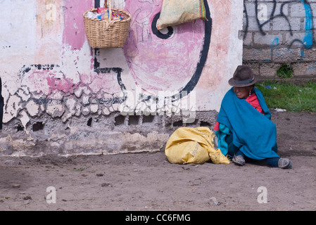 Une très vieille femme indienne andine est assis sur le sol près d'un mur de graffiti marqué Saquisili, Equateur, Amérique du Sud. Banque D'Images