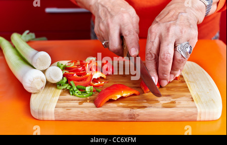 Senior woman mains hacher les légumes sur une planche en bois dans la cuisine Banque D'Images