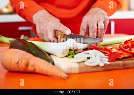 Senior woman mains hacher les légumes sur une planche en bois dans la cuisine Banque D'Images