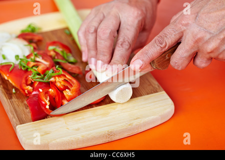 Senior woman mains hacher les légumes sur une planche en bois dans la cuisine Banque D'Images