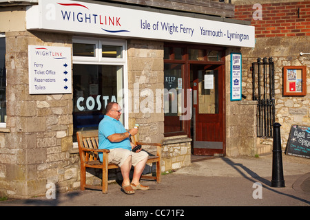 Homme mûr assis sur un banc en profitant d'une glace à l'extérieur du bureau de ferry de Wightlink à Yarmouth, île de Wight, Hampshire Royaume-Uni en septembre Banque D'Images