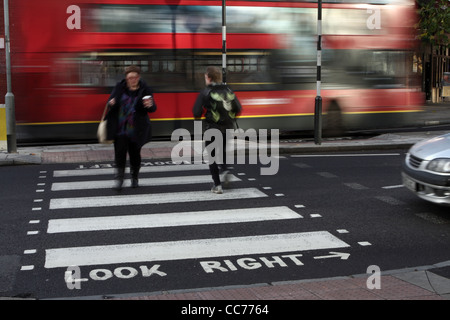 Une femme tenant un verre marche à travers un passage piétons à Londres en même temps qu'un jogger traverse en sens inverse Banque D'Images