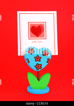 Carte vierge avec coeur rouge et fleur titulaire isolé sur fond rouge, conceptual image d'amour et de la Saint-Valentin Banque D'Images