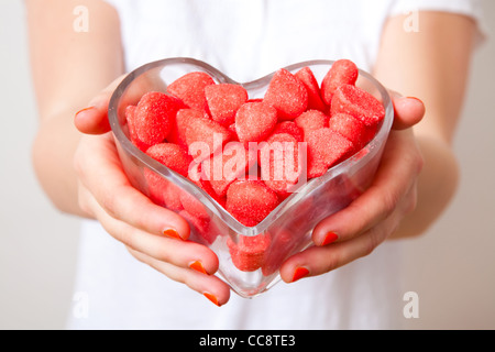 Femme offrant des bonbons rouges à partir d'un bol en forme de coeur. Studio shot. Banque D'Images