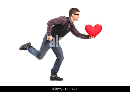 Un jeune homme qui court avec un oreiller en forme de cœur rouge dans sa main Banque D'Images