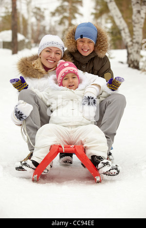 Enfants heureux et leur mère assis sur un traîneau dans park Banque D'Images