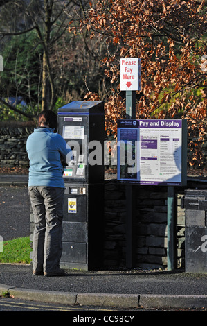 Femme à l'aide de payer et afficher un parcomètre. Grasmere, Parc National de Lake District, Cumbria, Angleterre, Royaume-Uni, Europe. Banque D'Images