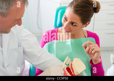 Dentiste expliquant le brossage des dents avec un patient à l'ensemble des dents artificielles Banque D'Images