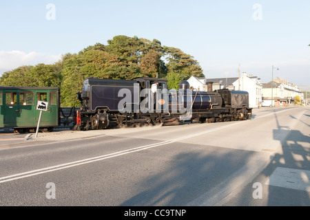 Une locomotive à vapeur avec un train de voyageurs sur la ligne qui traverse la Welsh Highland Road à Porthmadog Banque D'Images