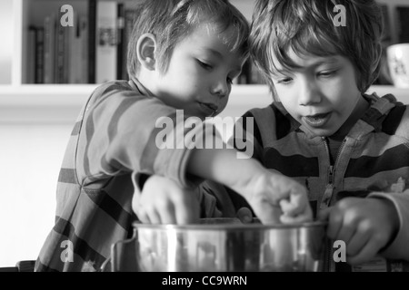 Deux jeunes garçons la confection d'un gâteau au chocolat - lécher le mélange à gâteau hors du bol Banque D'Images