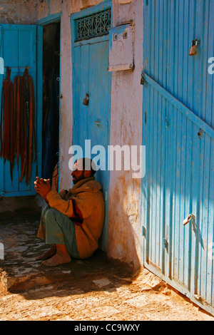 Un homme qui prie sur le sol devant sa boutique. Chefchaouen, Maroc. Banque D'Images