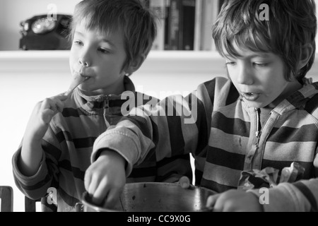 Deux jeunes garçons la confection d'un gâteau au chocolat - lécher le mélange à gâteau hors du bol Banque D'Images