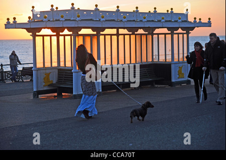 Les gens en passant devant un refuge au cours d'un spectaculaire coucher de soleil le long du front de mer de Hove Sussex UK Banque D'Images
