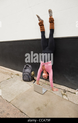 Woman performing handstand et using laptop on pavement Banque D'Images