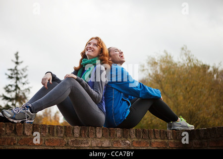 Les jeunes femmes assis dos à dos sur mur de brique Banque D'Images