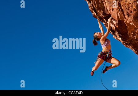 Female rock climber luttes de falaise pour sa prochaine prise sur une ascension difficile. Banque D'Images