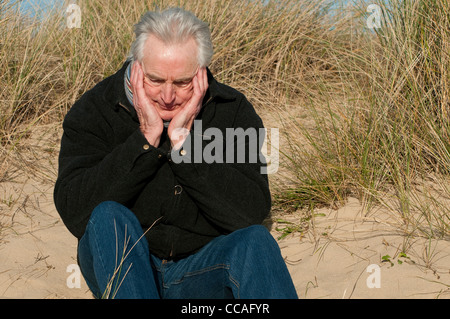 Déprimé senior male sitting on beach Banque D'Images