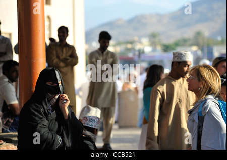 Une femme européenne, devant une femme, habillée en noir Bedu portant son masque traditionnel au marché de dimanche ; Nizwa Banque D'Images