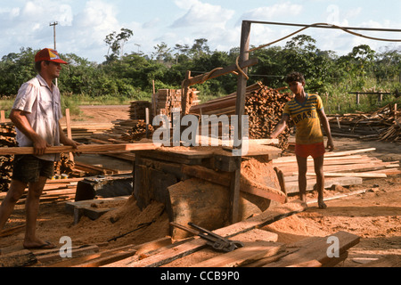 L'État de Para au Brésil. Bois de scierie cour pleine de sciages ; deux hommes portant des tongs en bois d'alimentation par le biais d'une machine couverte de rabotage dans la sciure de bois à l'air libre ; grand monkey clés sur le terrain - très désordonnée et dangereuse. Banque D'Images