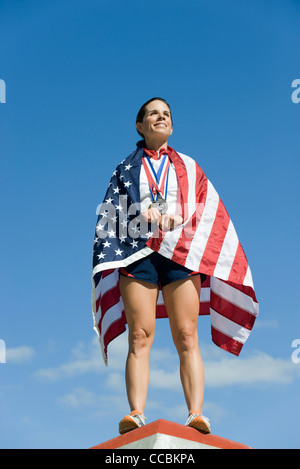 Athlète féminin à l'honneur sur le podium, enveloppé dans un drapeau américain Banque D'Images